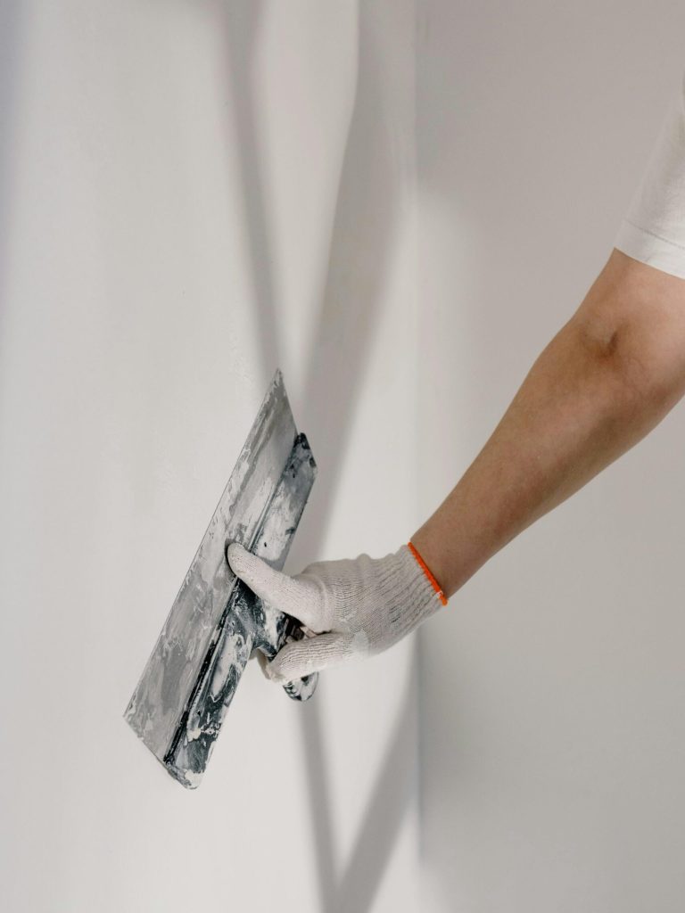 Crop anonymous male worker in gloves holding putty knife while working at home
